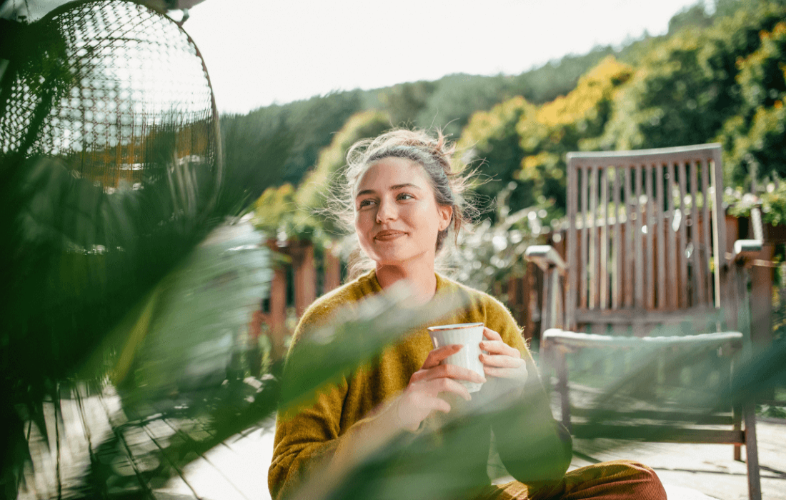 Eine Frau sitzt entspannt im Schneidersitz auf einer Holzterrasse.