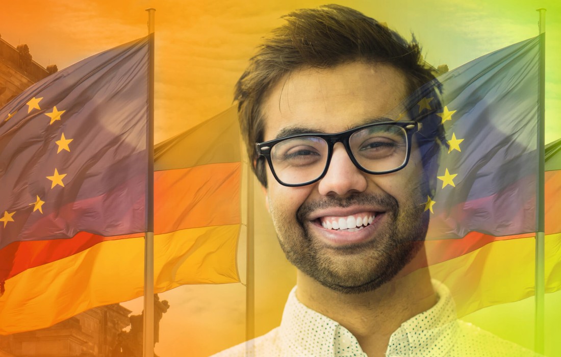 Ein Mann mit Brille lächelt in die Kamera. Hinter ihm wehen die deutsche Glagge und die Flagge der Europäischen Union.